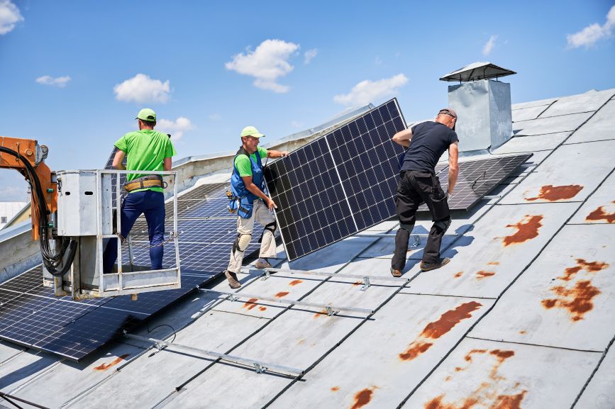 Team of workers removing solar panels from a rusty metal rooftop during maintenance