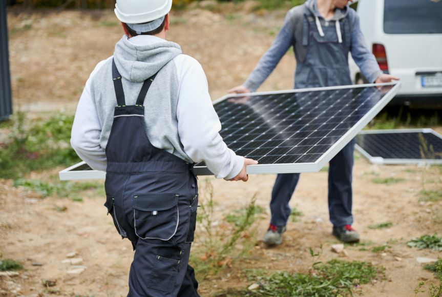 Technicians carrying a solar panel during removal and reinstallation by First Solar Installers, representing companies that remove and reinstall solar panels.