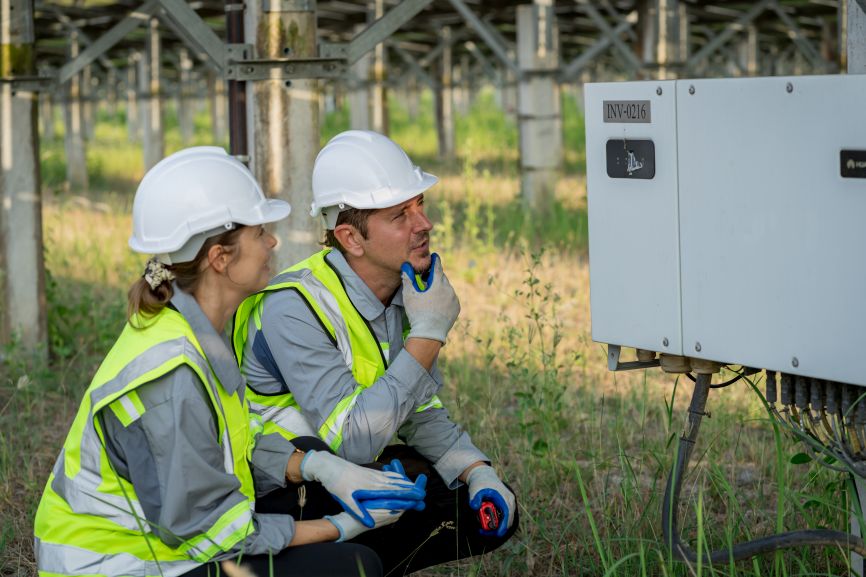 Engineers inspecting a solar inverter at a solar farm, demonstrating equipment used in String vs. Microinverters vs. Hybrid systems by First Solar Installers.